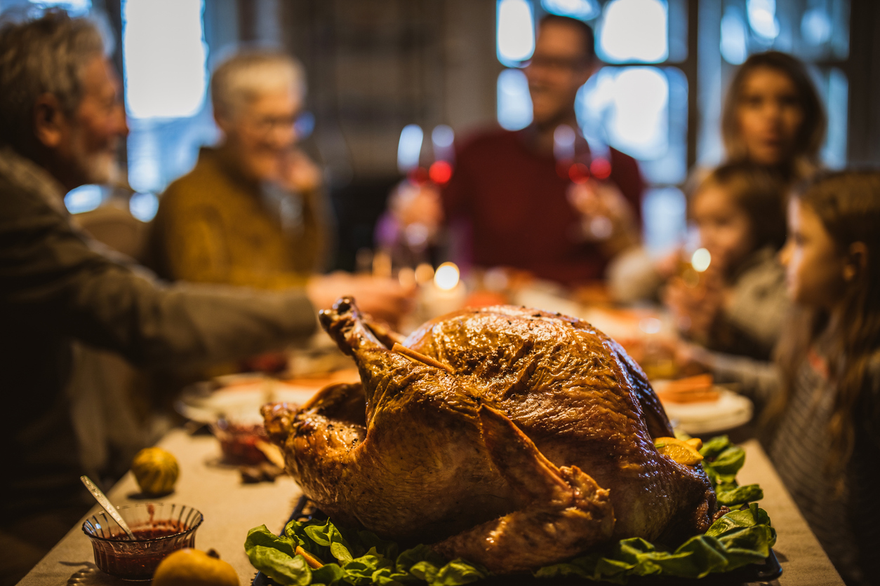 Family sits down for thanksgiving dinner, focused shot on the turkey.
