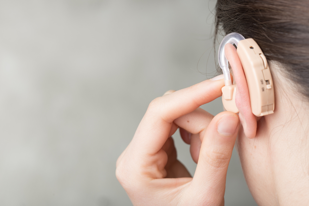 Close up of a woman with her hand by her ear, adjusting her hearing aid volume. 