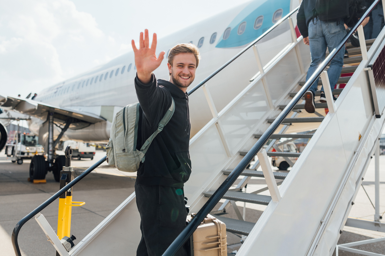 Happy man with a backpack waving and climbing the stairs onto a small plane.