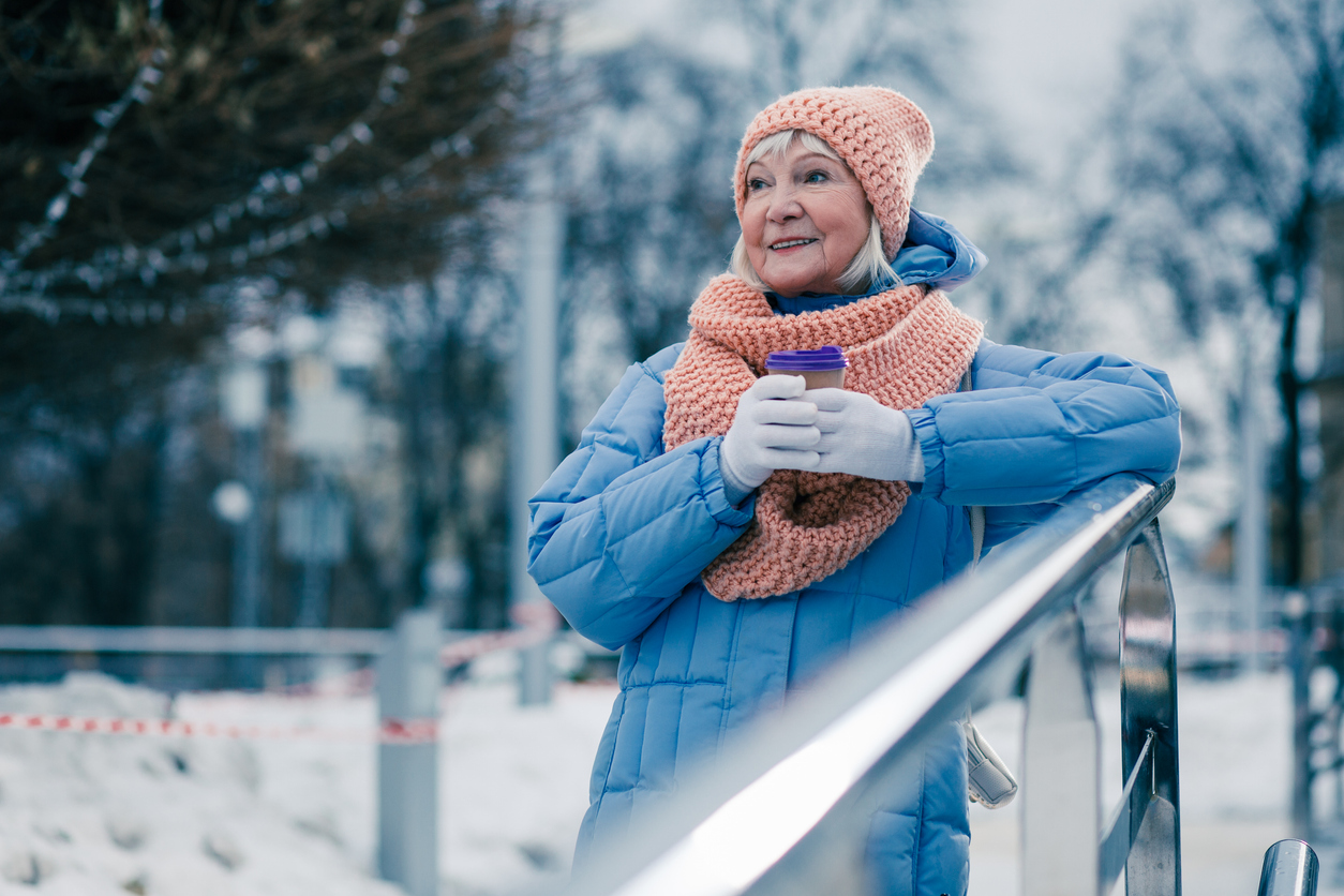Woman in scarf and hat drinking coffee in a snowy park