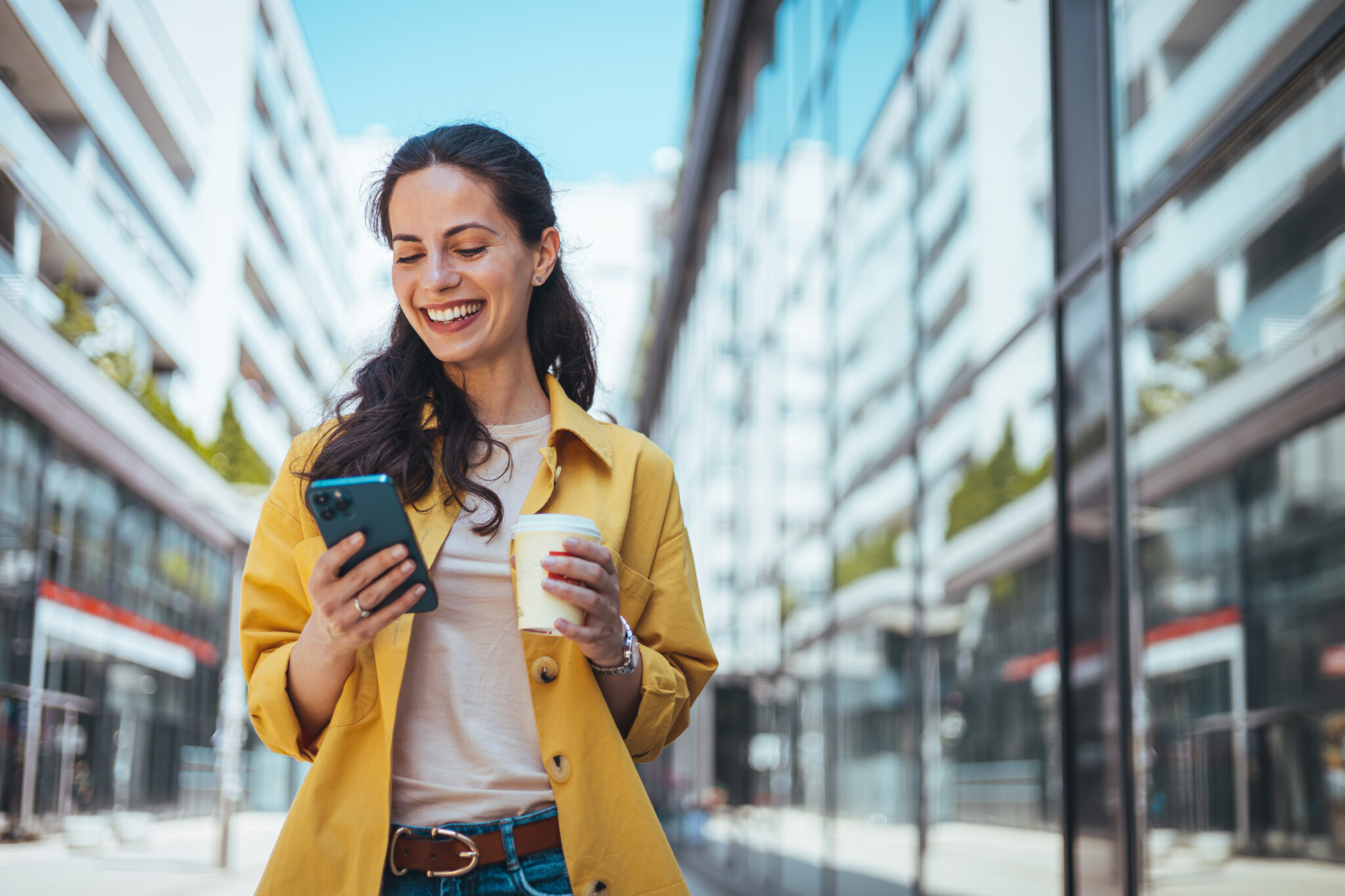 Woman in the city: walking down the city streets with a coffee and her phone.
