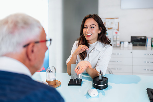 Audiologist is presenting a hearing aid device to a senior patient during a consultation in a modern audiology clinic, discussing options for improving hearing health