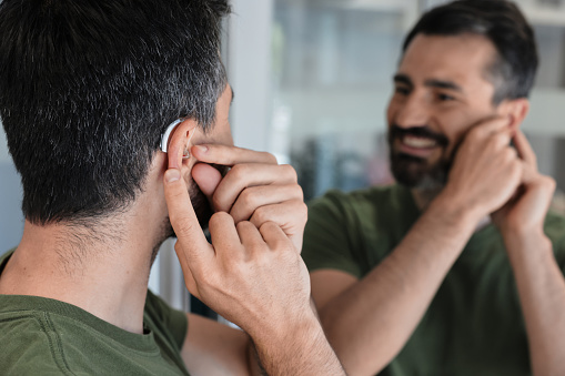 Smiling man reinserts his hearing aid after completing a cleaning routine.