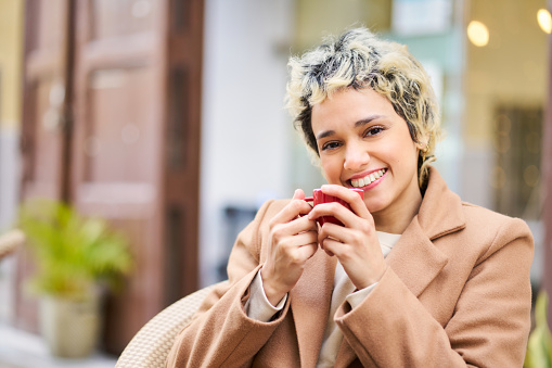 Smiling person at an outdoor cafe holding a cup of tea.