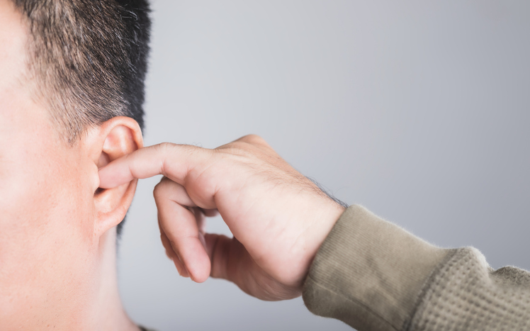 A close-up of a man using his finger to scratch inside his ear, highlighting the risks of ear irritation and injury from ear picking. This image emphasizes the importance of safe ear care practices