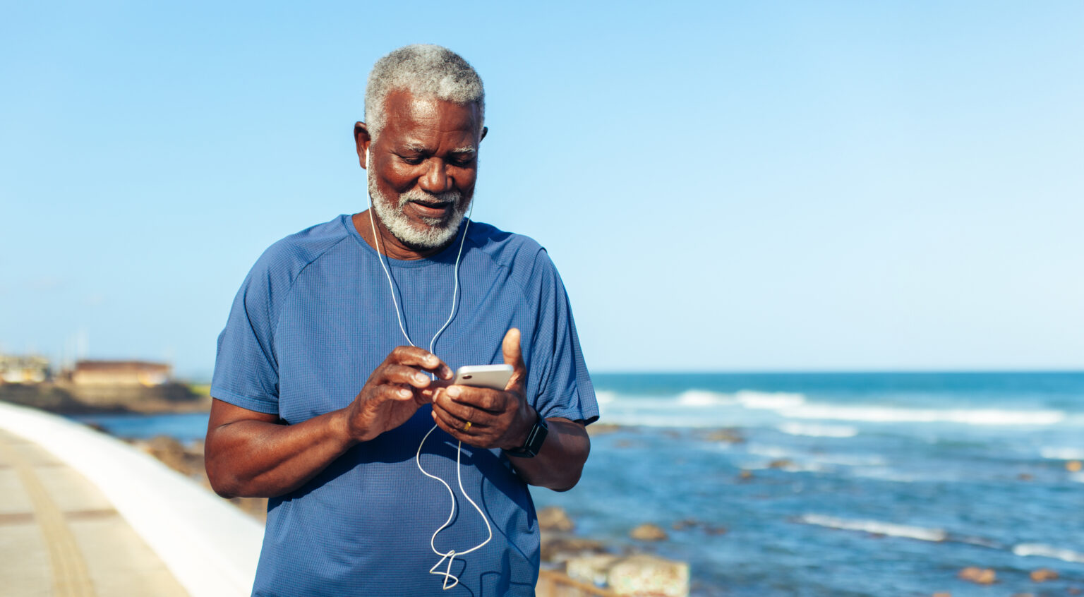 Older man staying active, going for a jog on the Maine coast. He is wearing headphones and turning on music before going for a run.
